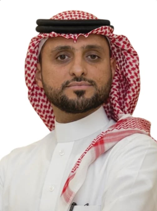 Portrait of a man wearing traditional Saudi Arabian clothing including a white thobe and red and white ghutra headscarf with black aqal